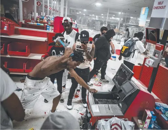  ?? Picture: AP ?? A looter targets a cash register at a Target store in Minneapoli­s as rioting engulfed the city of St Paul for a second night.