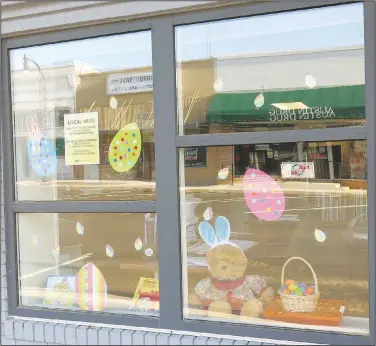  ?? (NWA Democrat-Gazette/Susan Holland) ?? A display in the windows at the Gravette Public Library features several decorative paper eggs and a little brown bear wearing his bunny ears and sitting beside his Easter basket. Designs for the Easter coloring contest were available at the library.