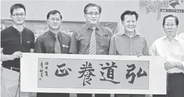  ??  ?? Huang (left) presents calligraph­y by a Yu Tian student to Lau (right).