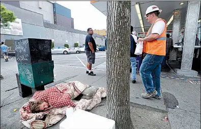  ?? AP ?? A man sleeps on the sidewalk as people line up to buy lunch at a Dick’s Drive-In in Seattle in May. The Seattle City Council has repealed a month-old tax on large employers that was intended to fund programs for the homeless.