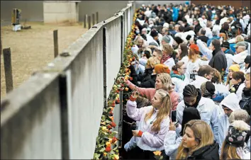  ?? MARKUS SCHREIBER/AP ?? People put roses in remains of the Berlin Wall during a ceremony to celebrate the 30th anniversar­y of its fall at the Wall memorial site Saturday at Bernauer Strasse in Berlin.