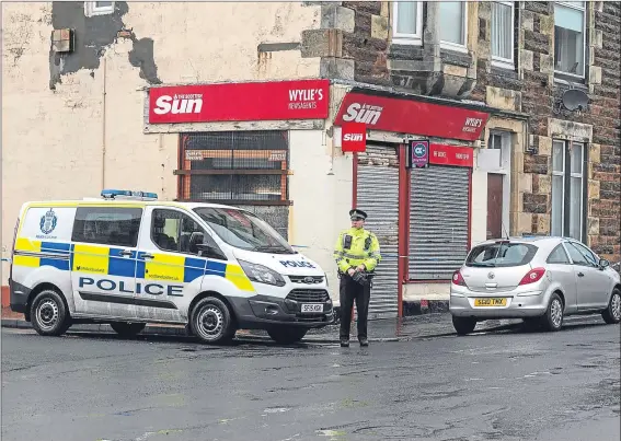  ??  ?? A policeman stands guard outside Wylie’s Newsagents in Saltcoats, where a pensioner collapsed and died after rushing to the aid of his partner