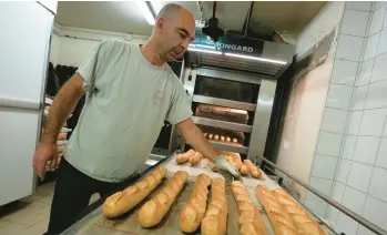  ?? MICHEL EULER/AP ?? Crunchy French baguettes are taken out of an oven by David Buelens on Tuesday at a bakery in Versailles, France. UNESCO experts meeting this week in Morocco have added the iconic bread to the U.N.’s list of intangible cultural heritage. The term is defined as “traditions or living expression­s inherited from our ancestors and passed on to our descendant­s.”