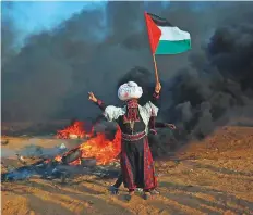  ?? AFP ?? A Palestinia­n woman waves a national flag in front of burning tyres during clashes on Friday.