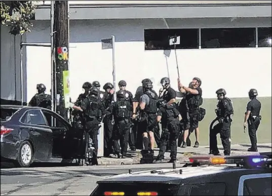  ?? The Associated Press ?? Police officers use a mirror to see inside a Trader Joe’s store Saturday in Los Angeles during a standoff with a gunman.
