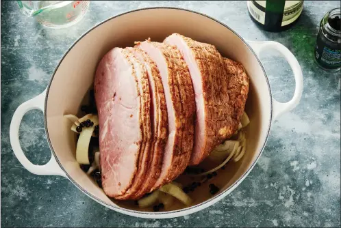  ?? (The New York Times/Bobbi Lin) ?? Steaming a ham on a rack of onions in white wine sweetened with honey and fragrant with juniper berries and cloves keeps the meat juicy and infuses it with flavor.