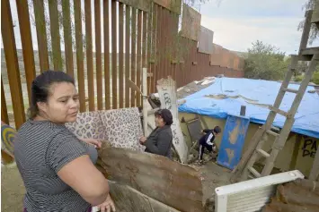  ?? (AP Photo/Gregory Bull) ?? In this Jan. 16, 2019, image, Yuli Arias, left, stands near a newly-replaced section of the border wall as her mother, Esther Arias, center, stands in the family's house that was once threatened by constructi­on along the border in Tijuana, Mexico. The U.S. faces a delicate dance as it charts a course to extend or replace border barriers near homes and structures.