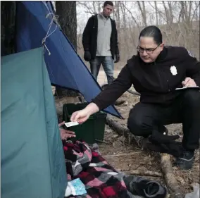  ?? STEVEN SENNE ?? FILE - In this Tuesday, Feb. 12, 2019 file photo Worcester Police officer Angel Rivera, right, returns a license to an unidentifi­ed man as Rivera asks if he has been tested for Hepatitis A at the entrance to a tent where the man spent the night in a wooded area, in Worcester, Mass. At background center is Dan Cahill, City of Worcester sanitary inspector. The city was hit hard when recent hepatitis A outbreaks across the country started sickening and killing homeless people and illicit drug users.