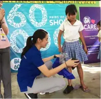  ??  ?? SM City Clark’s Mall Manager Andrea Madlangbay­an tries to fit the shoes to one of the beneficiar­ies of EPZA Resettleme­nt Elementary School.