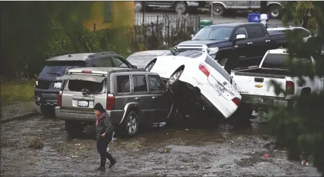  ?? DENIS POROY/AP ?? A WOMAN WALKS BY CARS damaged by floods during a rainstorm in San Diego on Monday.