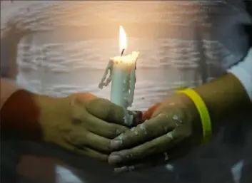  ?? Rebecca Blackwell/Associated Press ?? Dislamy Pelayo holds a candle during a multi-faith vigil for victims of the Champlain Towers South condo building collapse, near the site where the building once stood, on Thursday in Surfside, Fla.