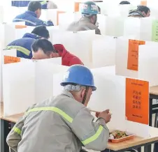  ??  ?? Workers have lunch at a dining hall using boards to separate people to prevent the spread of the new coronaviru­s in Yantai in China’s eastern Shandong province.