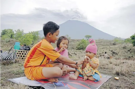  ?? FIRDIA LISNAWATI, THE ASSOCIATED PRESS ?? With the erupting volcano of Mount Agung looming behind them, children await their parents who are working in a a field in Karangasem, a regency of Bali, Indonesia.