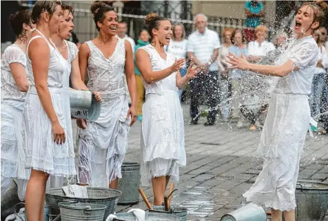  ??  ?? Es ist Waschtag am Elias Holl Platz. Die sechs Waschfraue­n vom Stuttgarte­r Straßenthe­ater „Laundry XL“pritscheln mit ihren Eimern und Wannen hemmungslo­s herum und verwandeln das Stadtbild mit ihren weißen Laken.