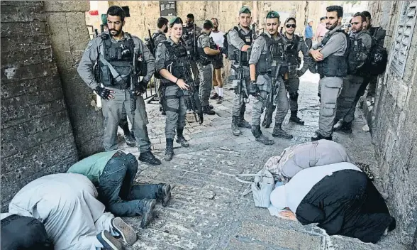  ?? ODED BALILTY / AP ?? Policías israelíes montan guardia en la puerta de los Leones de Jerusalén junto a unos palestinos que hacen allí mismo sus plegarias