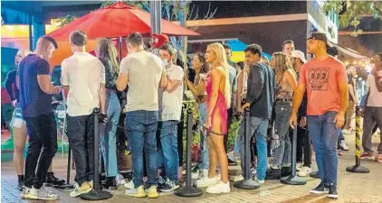  ?? JENNIFER LETT/SOUTH FLORIDA SUN SENTINEL ?? Few people wear masks as they wait in line outside Tin Roof and Honey in Delray Beach on Dec. 12.