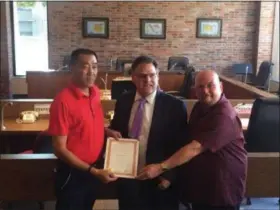  ?? KEVIN MARTIN — THE MORNING JOURNAL ?? Lorain Council-at-Large member Mitchell Fallis, center, presents a framed resolution to Weijjun Zhao, left, and Jose William Vasquez on Sept. 21 in council chambers at 100 W. Erie Ave. The resolution formally welcomes the Zhao family from Beijing to...