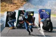  ?? Ronaldo Schemidt / AFP / Getty Images ?? Opposition activists take cover behind advertisem­ent placards as they clash with riot police Wednesday during a protest march in Caracas.