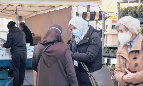  ?? SCHREIBER/AP MARKUS ?? Aliye Tuerkyilma­z, center right, a member of a multilingu­al team, speaks to a woman about the pandemic last week at a market in Berlin.