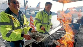  ?? AP ?? Airport operation workers wearing fluorescen­t safety jackets flipped burgers and hot dogs on a grill set up on the tarmac in front of a plane at Salt Lake City Internatio­nal Airport. Airport officials treated workers from the TSA, FAA and Customs and Border Protection to a free barbecue lunch as a gesture to keep their spirits up during the shutdown.