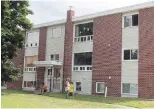  ??  ?? A family outside the Fredericto­n apartment building complex Tuesday where four people were killed on Friday, including two police officers. Bullet-hole evidence markers can be seen in the top window at centre.