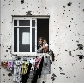  ??  ?? A mother holds her child while looking out from her Gaza City apartment badly damaged by artillary fire during the Israel–Gaza conflict also known as Operation Protective Edge.
