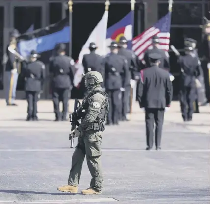  ??  ?? 0 A heavily armed officer patrols as a casket is unloaded at a memorial service for mass shooting victim Eric Talley