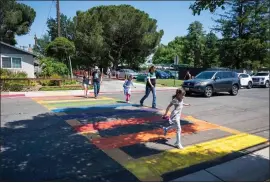  ?? LEZLIE STERLING — THE SACRAMENTO BEE ?? Parents and students cross the street while walking in a rainbow-colored crosswalk across from Birch Lane Elementary School in Davis on May 25, 2023. The crosswalk was painted that way for LGBTQ Pride Month.