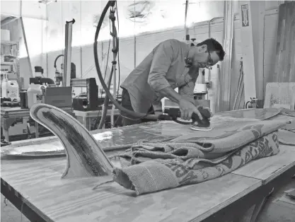  ?? PHOTOS BY DREW DAWSON/MILWAUKEE JOURNAL SENTINEL ?? Ted Burdett sands the belly of the bio-based surfboard, which is a composite made of coffee bags and palm leaves.