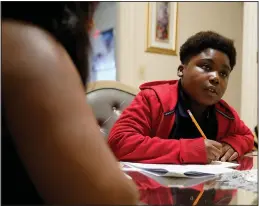  ?? (AP/Steven Senne) ?? Evena Joseph (left) sits with her son J. Ryan Mathurin, 10, as he does his homework Dec. 22 at their home in Boston.