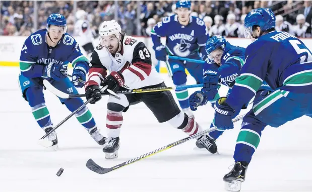  ?? —CP ?? Conor Garland of the Arizona Coyotes pushes the puck past Canucks checkers Nikolay Goldobin, Troy Stecher, and Derrick Pouliot during the first period on Thursday night at Rogers Arena. Garland scored for the visitors as they edged the Canucks 4-3 in overtime.