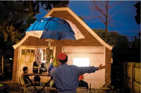  ?? E. JASON WAMBSGANS/CHICAGO TRIBUNE PHOTOS ?? Joey Garfield checks for rain while projecting 16mm films borrowed from the Chicago Film Society projector loan program in his backyard on May 15.