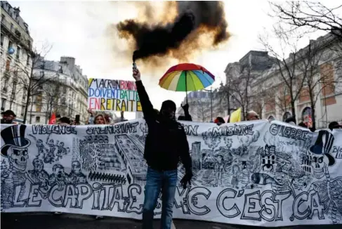  ?? (AFP via Getty) ?? A protester holds a smoke bomb in front of an anti-capitalist banner during a demonstrat­ion in Paris yesterday