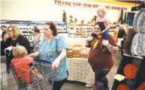  ?? STAFF PHOTO BY DOUG STRICKLAND ?? Brittany Mays, right, carries Kinley Mays as Teresa Gunnoe, left, pushes Kiara Mays in a cart Tuesday during the grand opening of Food City’s new location on Mission Ridge Road.
