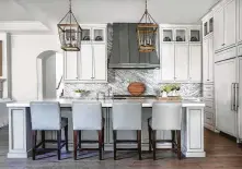  ??  ?? The Longs’ builder included current white cabinets and gray-veiny stone in the kitchen, so only new lighting in the form of large, lantern-style chandelier­s was needed.