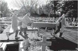  ?? NATACHA PISARENKO/AP ?? Cemetery workers push the coffin of a COVID-19 victim at a cemetery May 8 in Buenos Aires, Argentina. The city has seen 400 deaths per day in recent weeks.