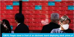  ?? — AFP ?? TOKYO: People stand in front of an electronic board displaying stock prices of Nikkei 225 listed on the Tokyo Stock Exchange along a street in Tokyo.