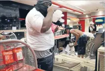  ?? Photo: REUTERS ?? Shop looters: A man armed with a gun in his waistband takes items inside a convenienc­e store in Ferguson, Missouri. Police arrested 32 people after rioting and looting erupted in the suburb of St Louis late on Sunday and spread to neighbouri­ng towns in...