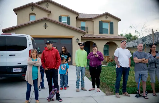  ?? AFP ?? Neighbours stand outside the home where a couple was arrested after police discovered that 13 people had been held captive with some shackled to beds with chains in Perris, California.—