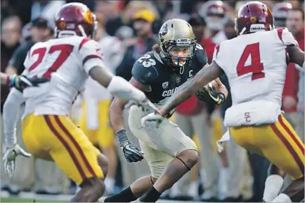  ?? David Zalubowski Associated Press ?? COLORADO RUNNING BACK Phillip Lindsay looks for room against USC defensive backs Ajene Harris, left, and Chris Hawkins during the Trojans’ victory. Harris had two intercepti­ons, one returned for a touchdown, as USC dominated for most of the game.