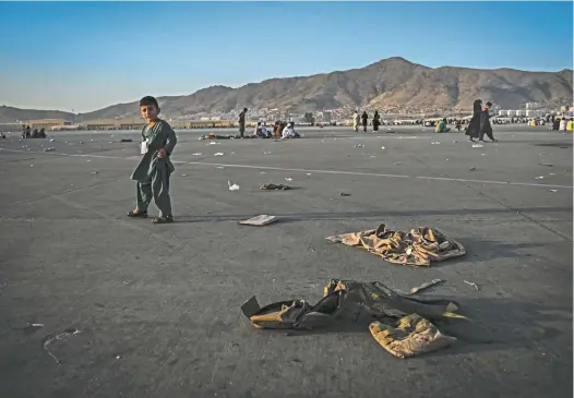  ?? Wakil Kohsar / AFP ?? An Afghan child walks near discarded military uniforms at Kabul airport this week.