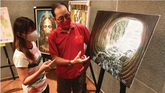 ?? ROBERTUS RISKY/JAWA POS ?? AIR TERJUN: Denny D’colo (kanan) menunjukka­n lukisannya yang terinspira­si aliran air terjun. Lukisannya dipamerkan oleh komunitas Surabaya Art Society (SAS) sejak Sabtu (1/8).