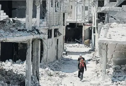  ?? ALAA AL-FAQIR / REUTERS ?? Una pareja camina por una calle en ruinas de la ciudad siria de Deera, donde entró en vigor el alto el fuego