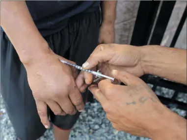  ?? STEVEN SENNE ?? FILE - In this Wednesday, Aug. 23, 2017file photo an unidentifi­ed heroin user, left, is injected by another man, right, on the street near a strip of land sometimes referred to as “Methadone Mile,” in Boston. Fatal drug overdoses in the U.S. were long known as being most common in big cities. That changed 13years ago, when Appalachia and other rural areas started seeing the nation’s highest overdose death rates. According to a government report released on Friday, Aug. 2, 2019, it’s shifted back again.