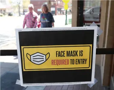  ?? The Sentinel-Record/Richard Rasmussen ?? ■ Pedestrian­s walk along the 600 block of Central Avenue near a sign on a business door requiring face masks for entry Monday.