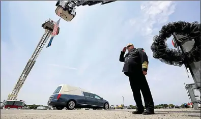  ?? Arkansas Democrat-Gazette/STATON BREIDENTHA­L ?? Batesville Fire Chief Brent Gleghorn salutes Friday in Newport as the hearse carrying Newport police Lt. Patrick Weatherfor­d passes under a flag hung between ladder trucks from the Batesville and Newport fire department­s.