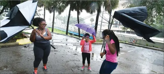  ?? The Associated Press ?? Umbrellas held by Janesse Brown, left, and her daughter Briana Johnson, 12, right, get torn apart by strong winds as Kyra Johnson, 8 watch, while they tried to visit Southbank Riverwalk in Jacksonvil­le, Fla. on Sunday as Hurricane Irma passed through...