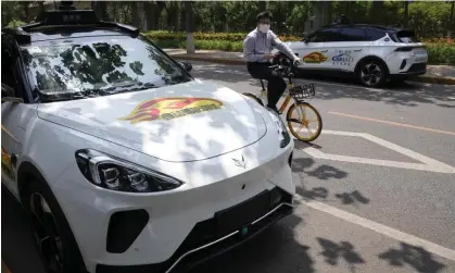  ?? ?? A man on a bicycle rides past self-driving taxis in Beijing. Photograph: Ng Han Guan/AP