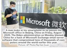  ?? Picture: AP Photo/Ng Han Guan ?? A man looks at his smartphone as he passes the Microsoft office in Beijing, China on Friday, August 7, 2020. The Biden administra­tion on Monday blamed China for a hack of Microsoft Exchange email server software that compromise­d tens of thousands of computers around the world earlier this year.