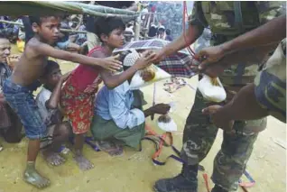  ??  ?? Refugees receive food packets at the refugee camp of Balukhali near Gumdhum on Monday.